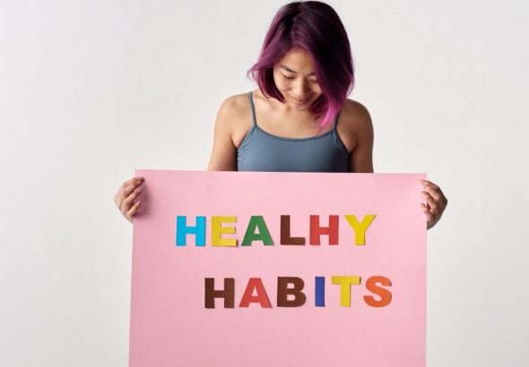 Asian woman holding a colorful 'Healthy Habits' sign in a studio setting, promoting wellness.