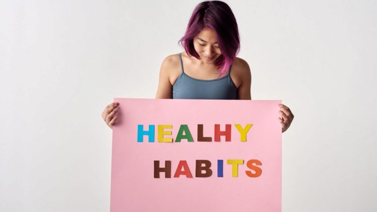 Asian woman holding a colorful 'Healthy Habits' sign in a studio setting, promoting wellness.