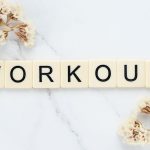 Letter tiles spelling 'WORKOUT' on marble with dried flowers, conveying fitness motivation.