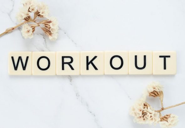 Letter tiles spelling 'WORKOUT' on marble with dried flowers, conveying fitness motivation.