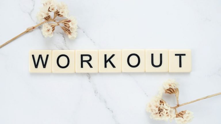 Letter tiles spelling 'WORKOUT' on marble with dried flowers, conveying fitness motivation.